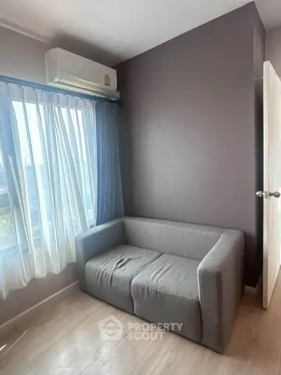 Cozy small living room with a gray sofa and natural light from large window.