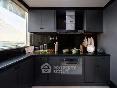Modern kitchen with sleek black cabinetry and built-in oven, featuring a large window with a view.