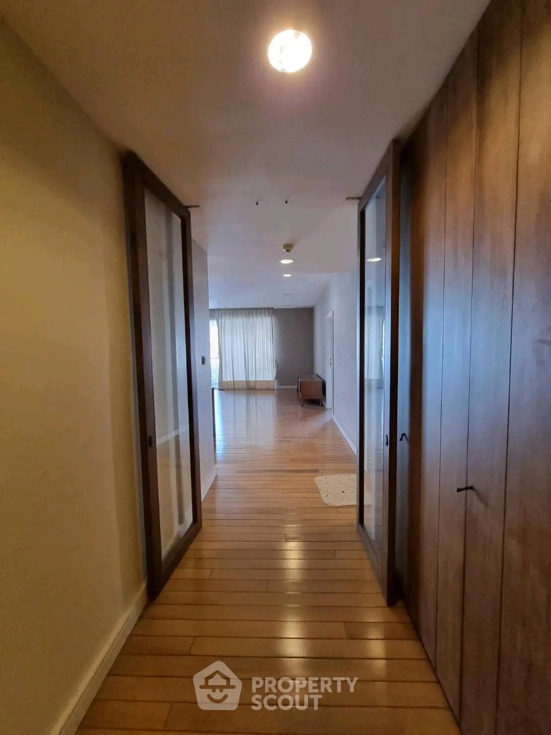 Spacious hallway with wooden flooring leading to a bright living area with large windows.