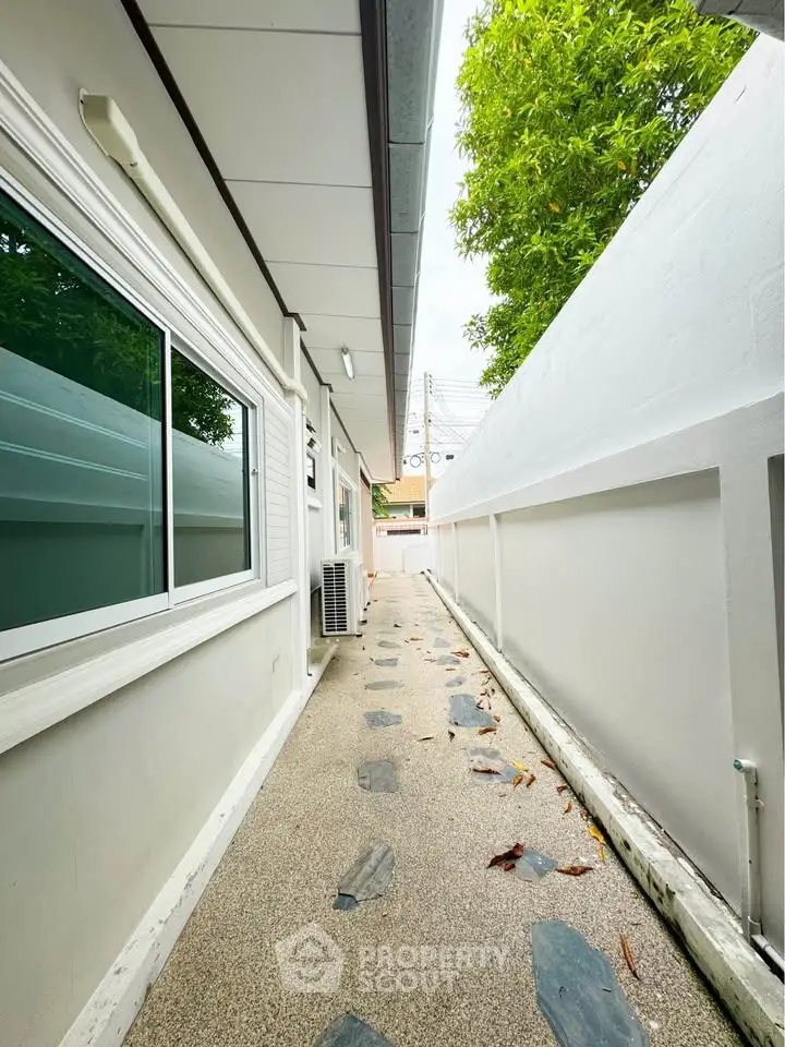 Charming side pathway with modern exterior and lush greenery, perfect for serene outdoor living.
