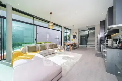 Luxurious open-plan living room with modern kitchen and stylish decor, featuring large windows and ample natural light.