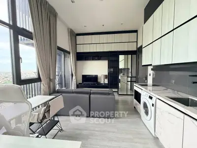 Modern living room with sleek kitchen and washing machine, featuring large windows and stylish decor.