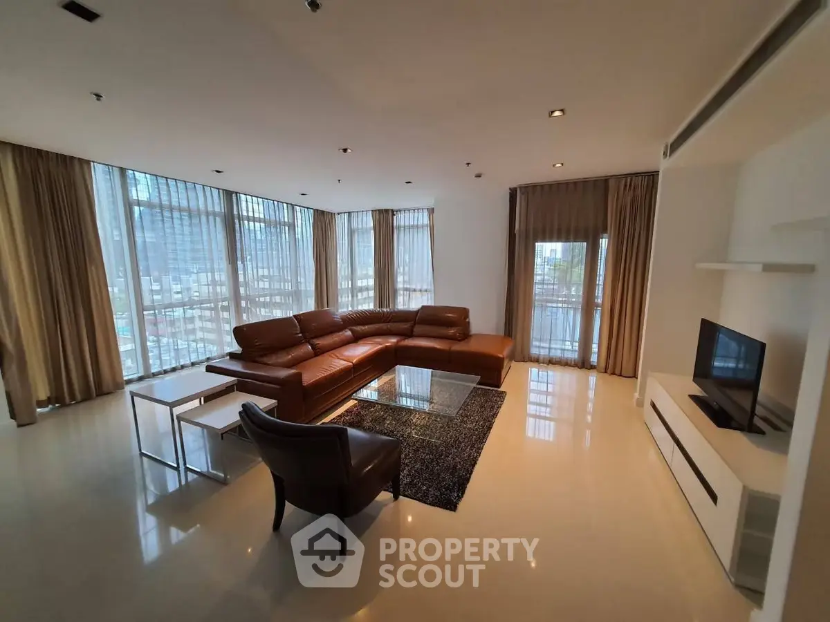 Spacious modern living room with leather sectional sofa and city view windows.