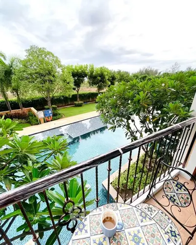 Charming balcony view overlooking lush garden and inviting pool, perfect for relaxation.