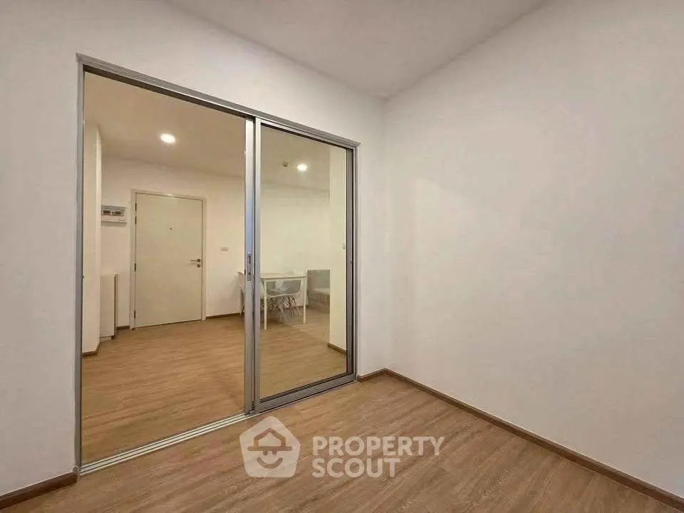 Spacious empty room with wooden flooring and sliding glass doors in modern apartment.