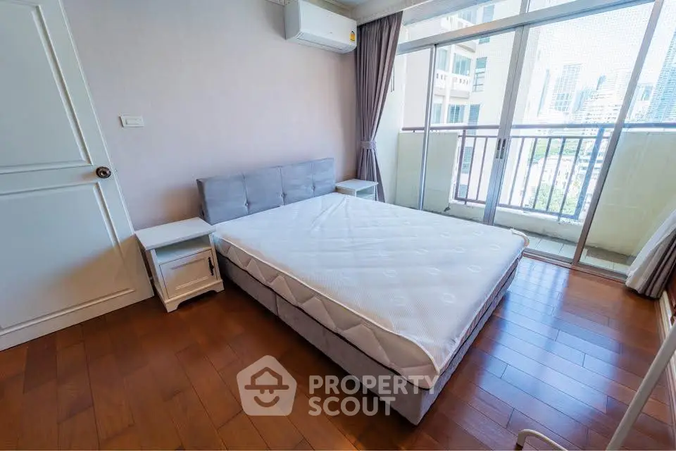 Spacious bedroom with balcony and city view, featuring hardwood floors and modern furnishings.