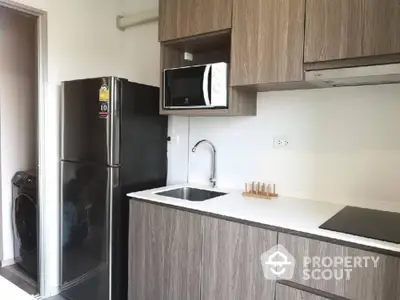 Modern kitchen with sleek cabinets, fridge, and microwave in stylish apartment.