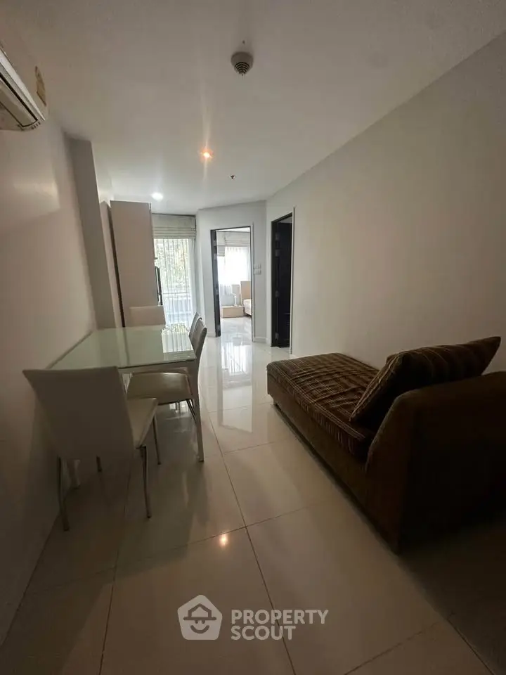 Modern apartment interior with sleek dining area and cozy seating, leading to a bright bedroom.