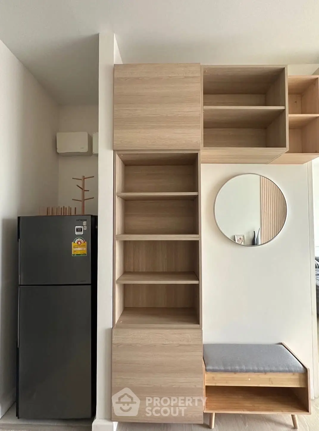 Modern interior with sleek storage and mirror, featuring a compact fridge and stylish wooden shelves.