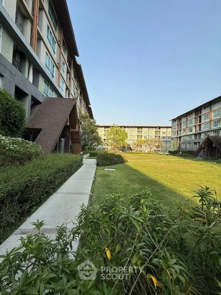 Modern apartment complex with lush green garden and clear blue sky.