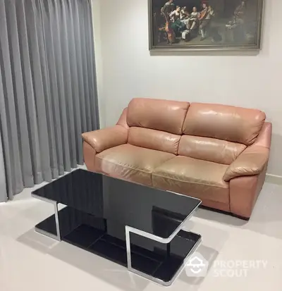 Elegant minimalist living room with a sleek beige leather sofa and a modern black glass coffee table, complemented by soft gray curtains and a classic painting.