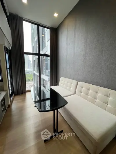 Modern living room with high ceiling and large windows offering city view.