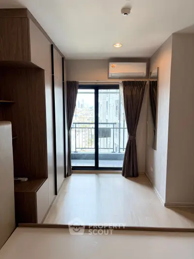 Modern apartment bedroom with balcony and city view, featuring sleek wooden cabinetry and air conditioning.