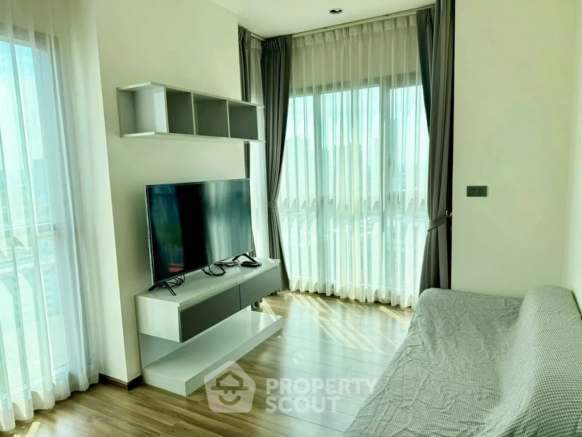 Modern living room with large windows and stylish TV setup, featuring elegant curtains and wooden flooring.
