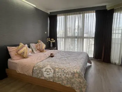 Spacious bedroom with large windows offering stunning city views, modern decor, and cozy ambiance.