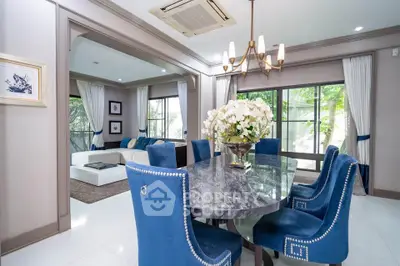 Elegant dining room with marble table and blue chairs, open to spacious living area with large windows.