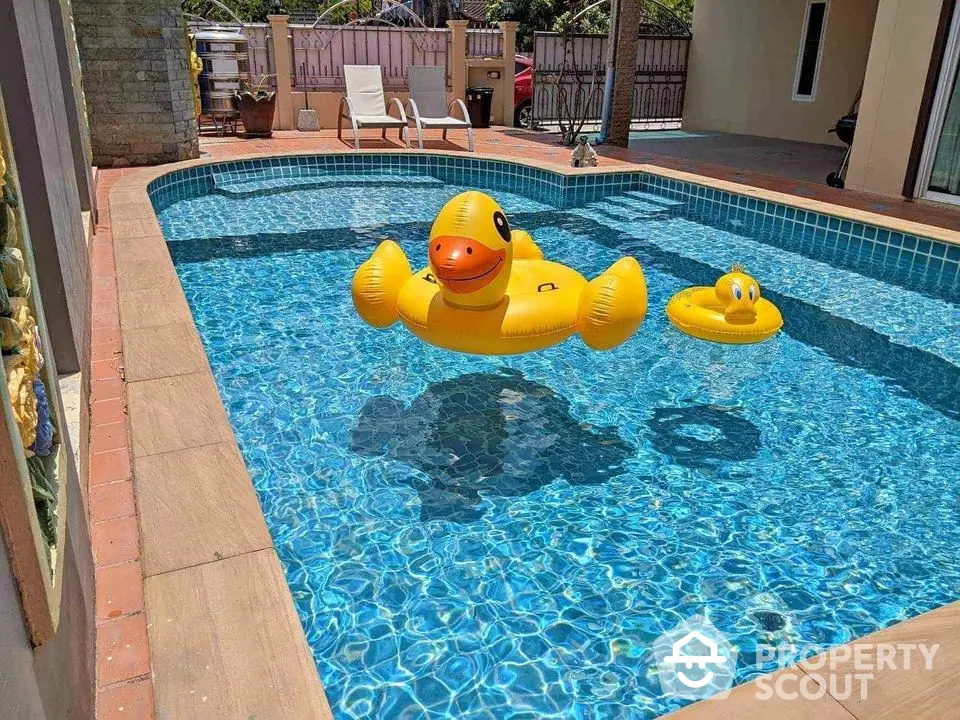 Luxurious private pool with playful inflatable duck floats in sunny backyard setting.