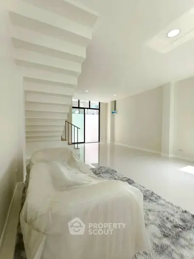 Spacious modern living room with sleek staircase and large windows for natural light.