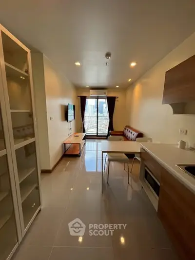 Modern living room with open kitchen and city view, featuring sleek furniture and natural light.