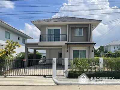 Modern two-story house with balcony and gated driveway in a suburban neighborhood.