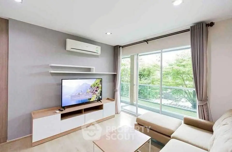 Modern living room with large windows and balcony view, featuring sleek furniture and air conditioning.