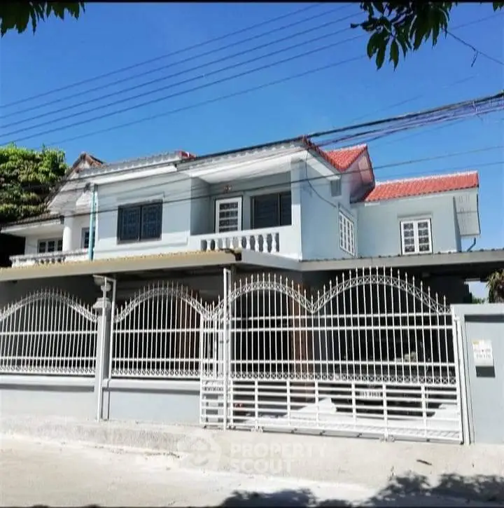 Charming two-story house with gated entrance and red roof in a serene neighborhood.