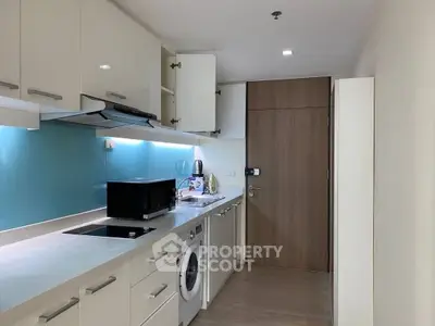 Modern kitchen with sleek cabinetry, washing machine, and microwave in compact layout.