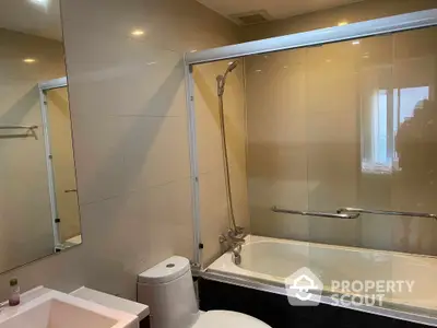 Modern bathroom with sleek bathtub and glass shower partition, featuring elegant tiling and well-placed lighting for a serene bathing experience.