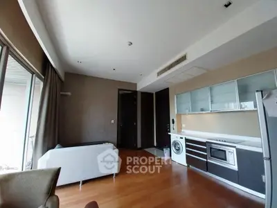 Modern living room with open kitchen, featuring sleek appliances and hardwood floors.