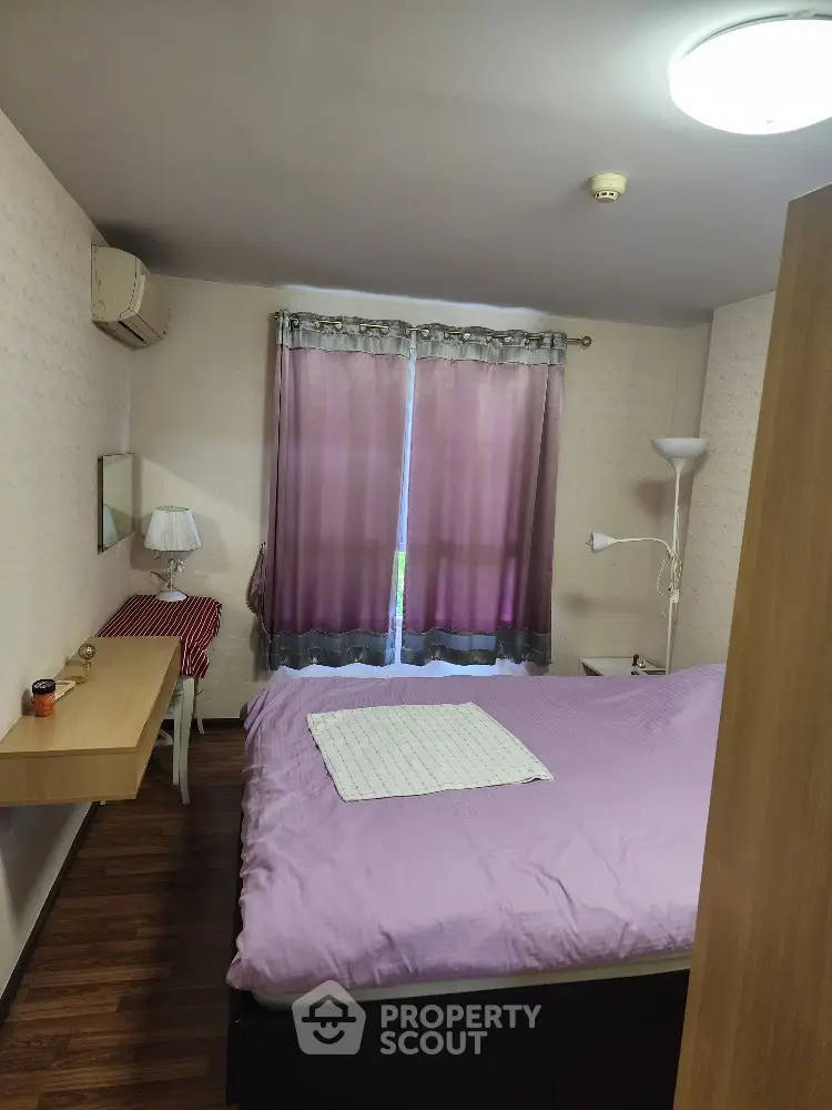 Cozy bedroom with hardwood flooring, large bed, and air conditioning unit, complemented by soft lighting and elegant curtains.