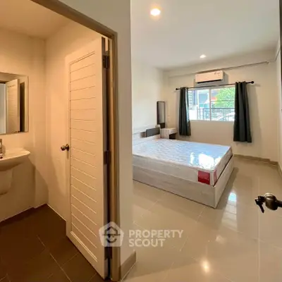 Spacious bedroom with ensuite bathroom in modern apartment, featuring large windows and air conditioning.