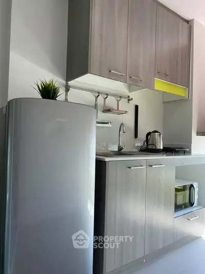 Modern kitchen with sleek cabinets, fridge, and microwave in compact layout.