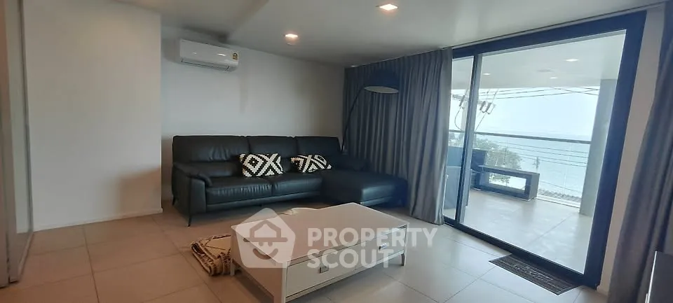 Modern living room with ocean view and balcony access, featuring sleek black sofa and stylish decor.