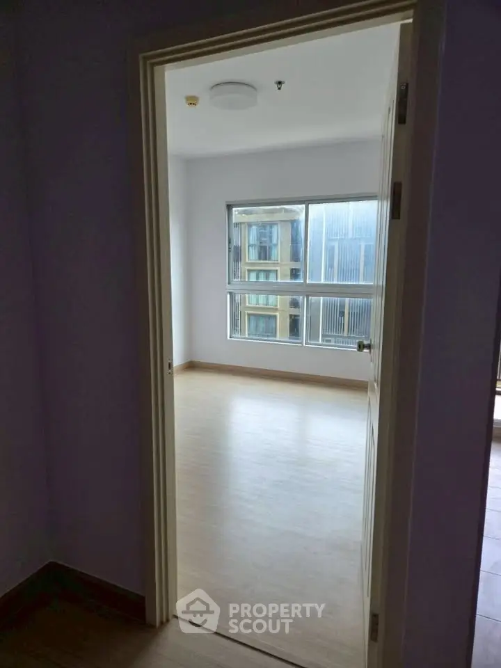 Spacious empty room with large window and wooden flooring, perfect for customization.