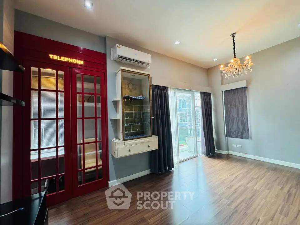 Stylish living room with unique red telephone booth feature and elegant chandelier lighting.