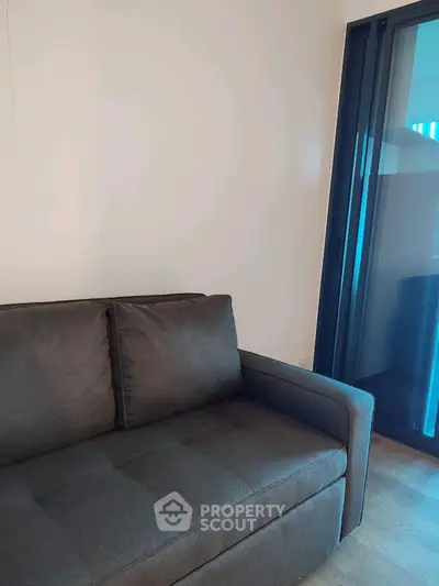 Modern living room with sleek dark sofa and large glass doors leading to balcony.