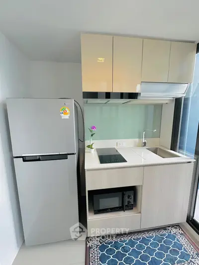 Modern compact kitchen with fridge, microwave, and sleek cabinetry