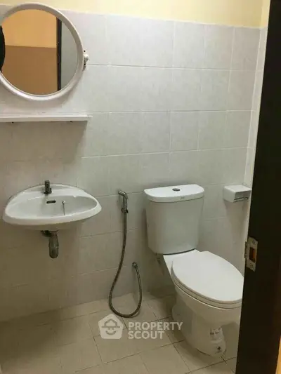 Compact bathroom with white tiles, sink, and toilet in a minimalist design.