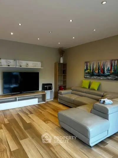 Modern living room with sleek furniture and stylish decor, featuring a large TV and wooden flooring.
