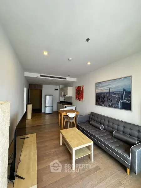Modern living room with open kitchen, stylish furniture, and cityscape artwork.