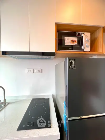 Modern kitchen with sleek appliances including a microwave, fridge, and electric cooktop.