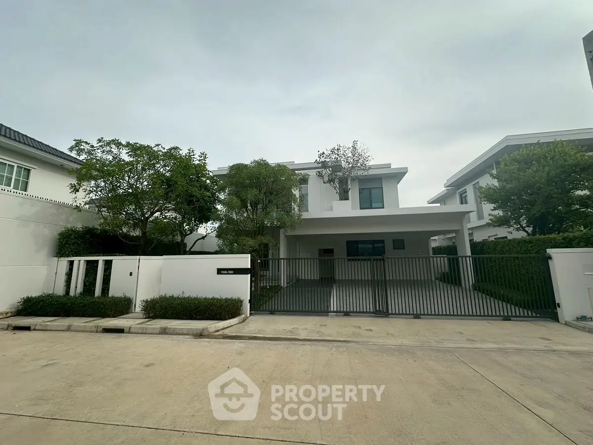 Modern two-story house with gated entrance and lush greenery in a serene neighborhood.