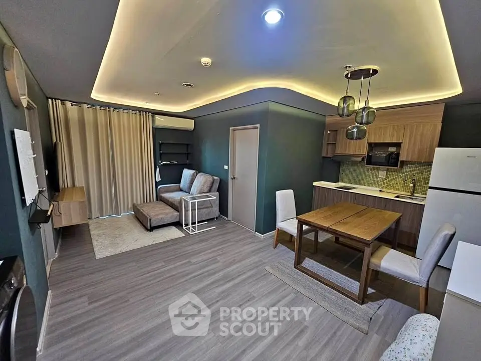 Modern open-plan living room with stylish kitchen and dining area, featuring sleek lighting and contemporary furniture.