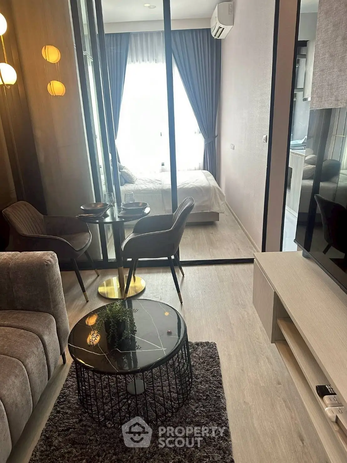 Modern living room with glass partition leading to a cozy bedroom, featuring stylish furniture and soft lighting.