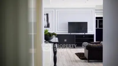 Elegant living room with modern decor and flat-screen TV, featuring stylish wall paneling and cozy seating.