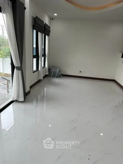 Spacious living room with large windows and elegant curtains, featuring glossy white tile flooring.