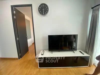 Modern living room with sleek TV stand and wall clock, featuring wooden flooring and natural light.