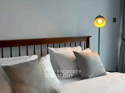 Cozy bedroom with stylish lamp and plush pillows, perfect for relaxation.