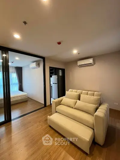 Modern living room with cozy sofa and view into bedroom, featuring sleek wooden flooring.
