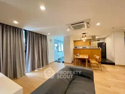 Spacious modern living room with open kitchen, wooden flooring, and stylish lighting.